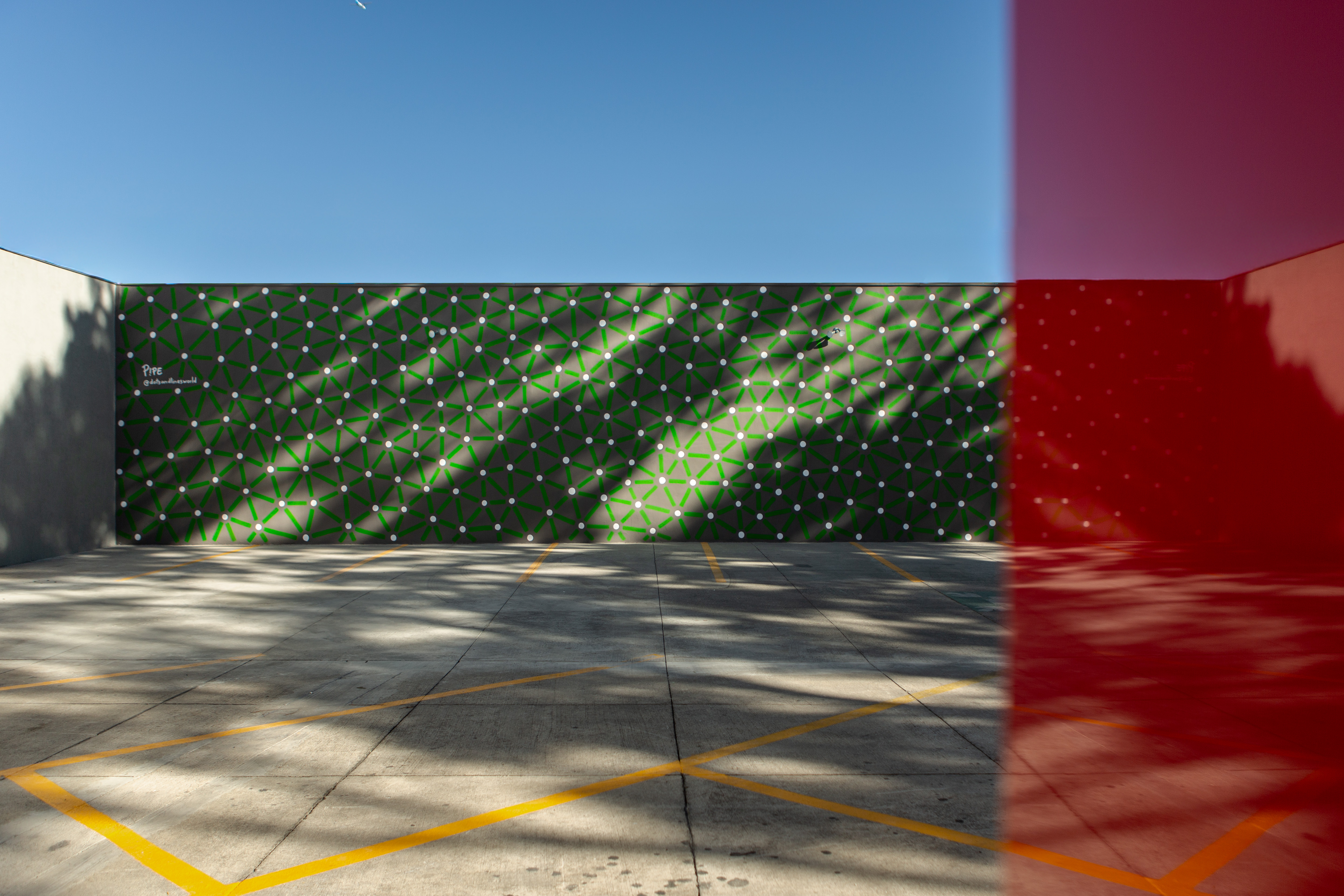 Roots: Courtyard with a red doorway and a long green-and-white patterned wall beneath a blue sky.