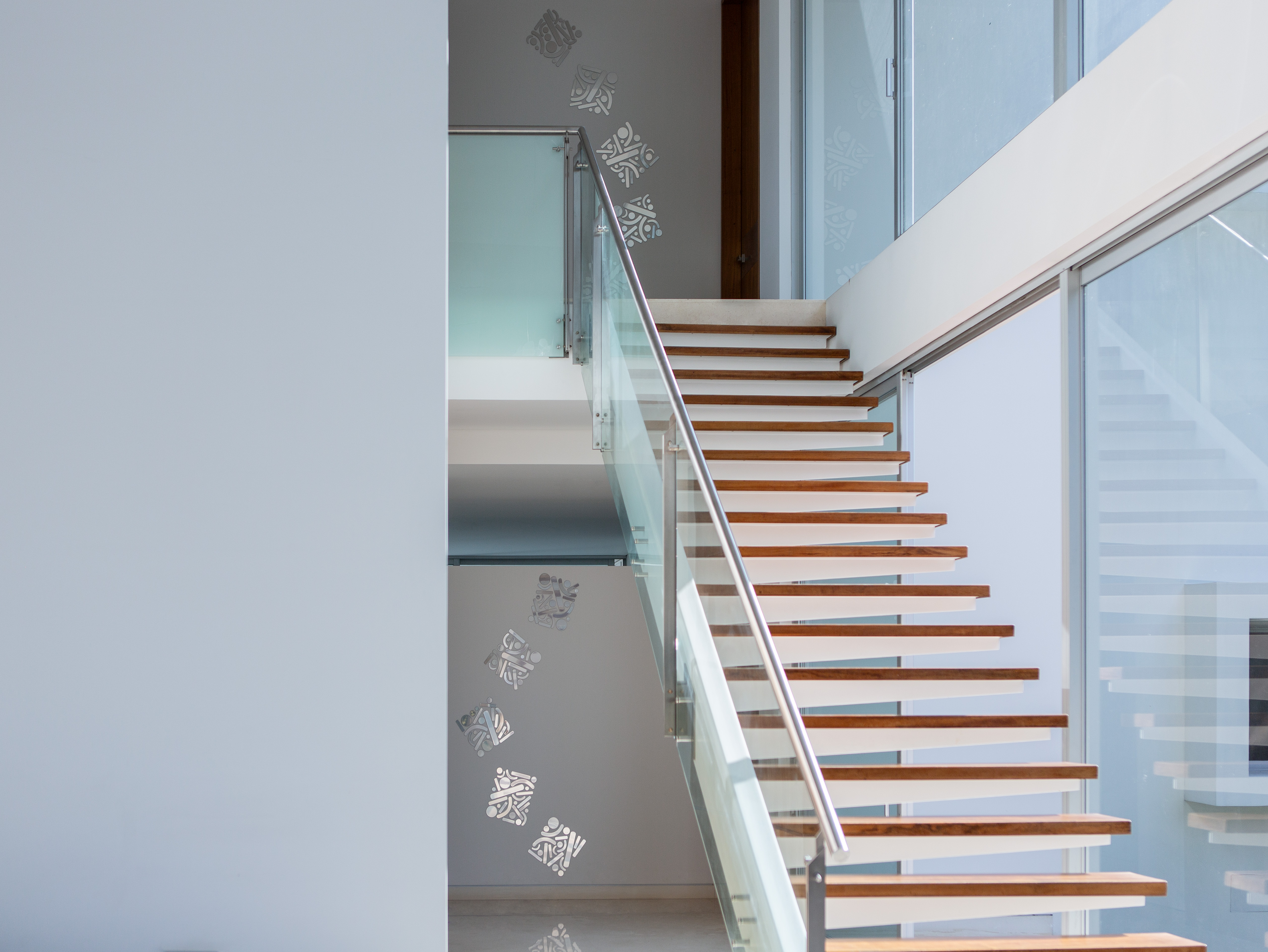 Continuity of Ideas: Tall wooden staircase and glass railing in a bright modern interior.
