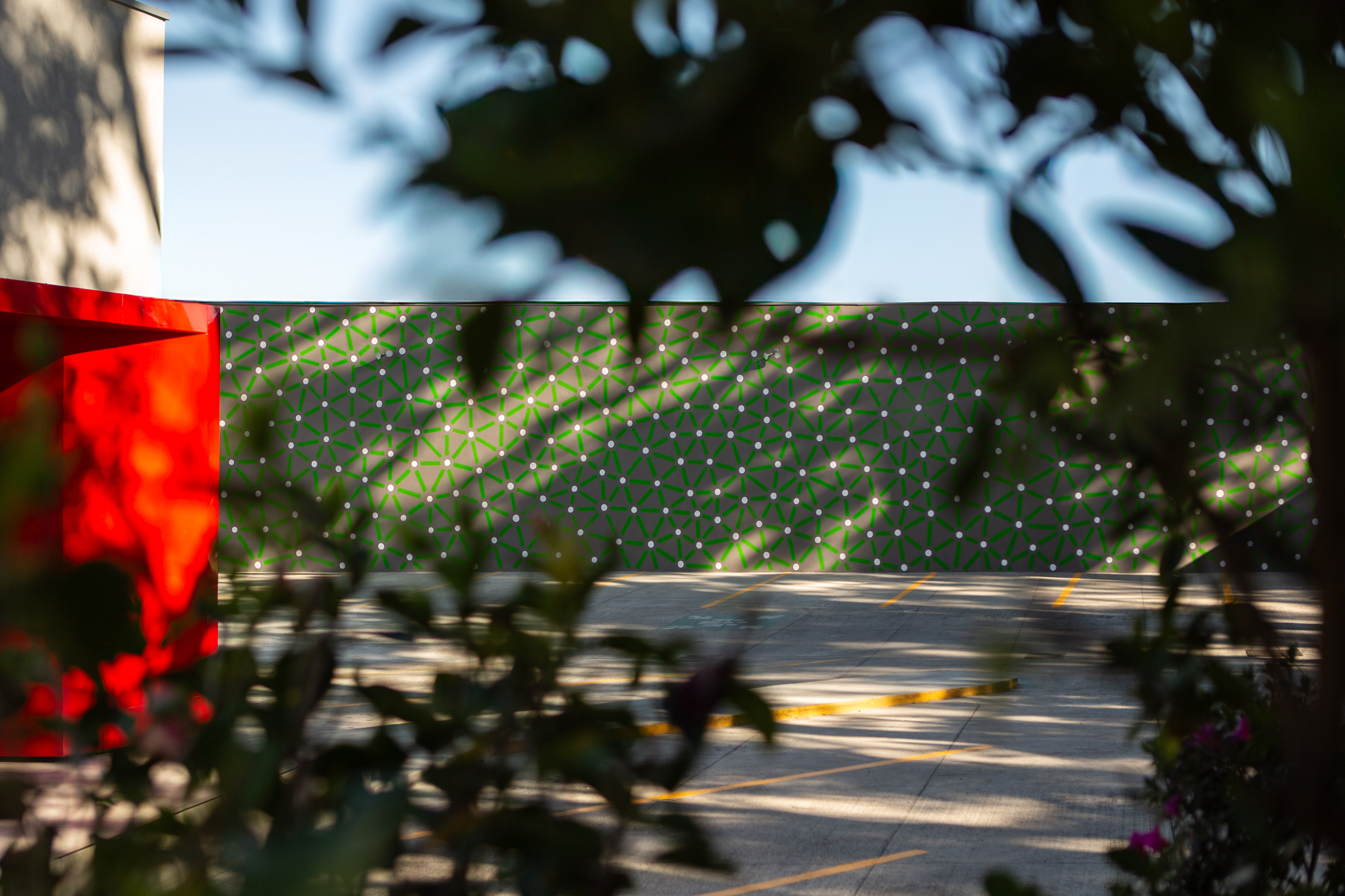 Sunlight and foliage cast shadows across green and white mural surfaces in a garden.