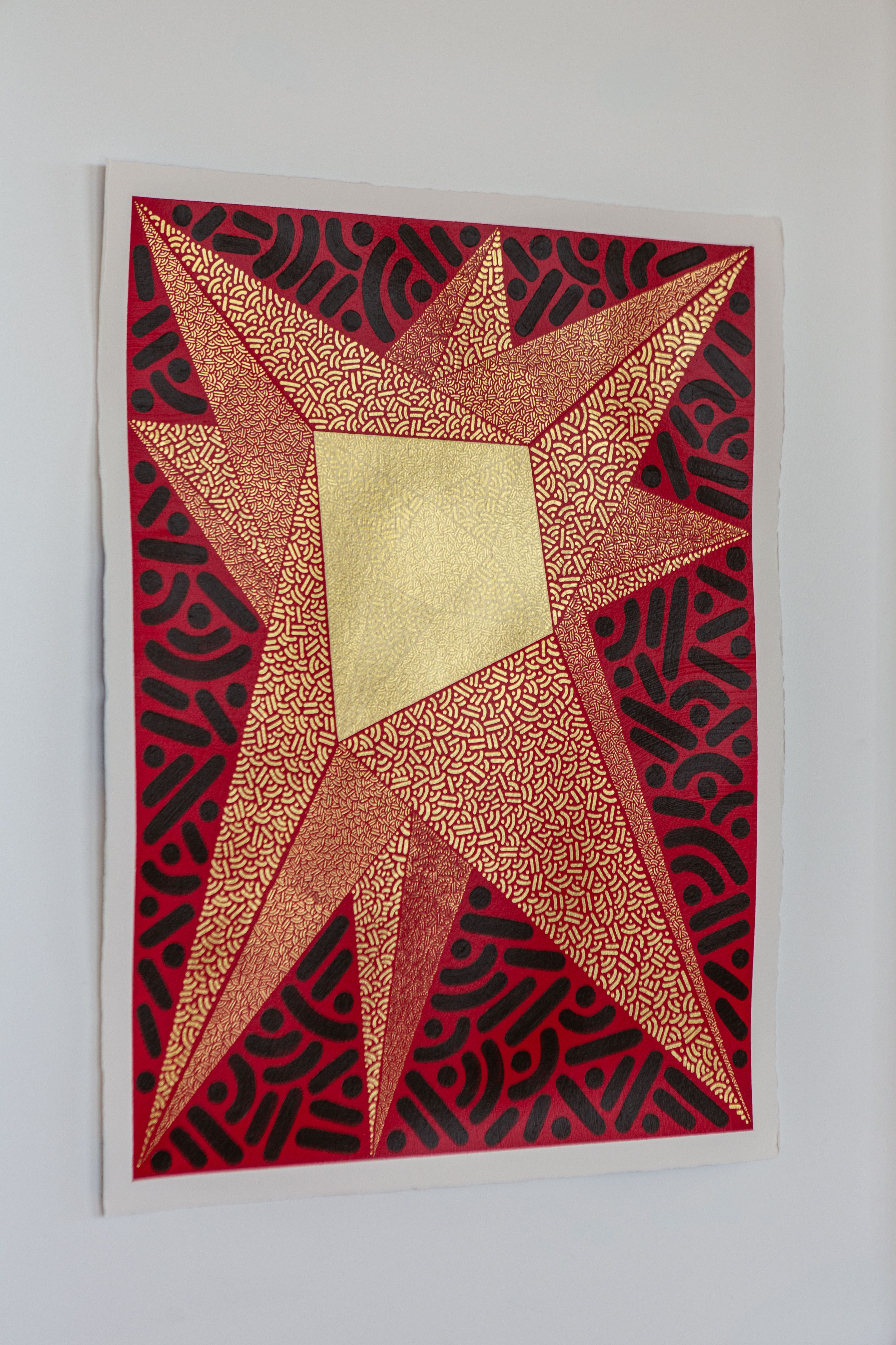 Radiant Convergence: Red, copper, and gold geometric artwork hanging on a pale wall.