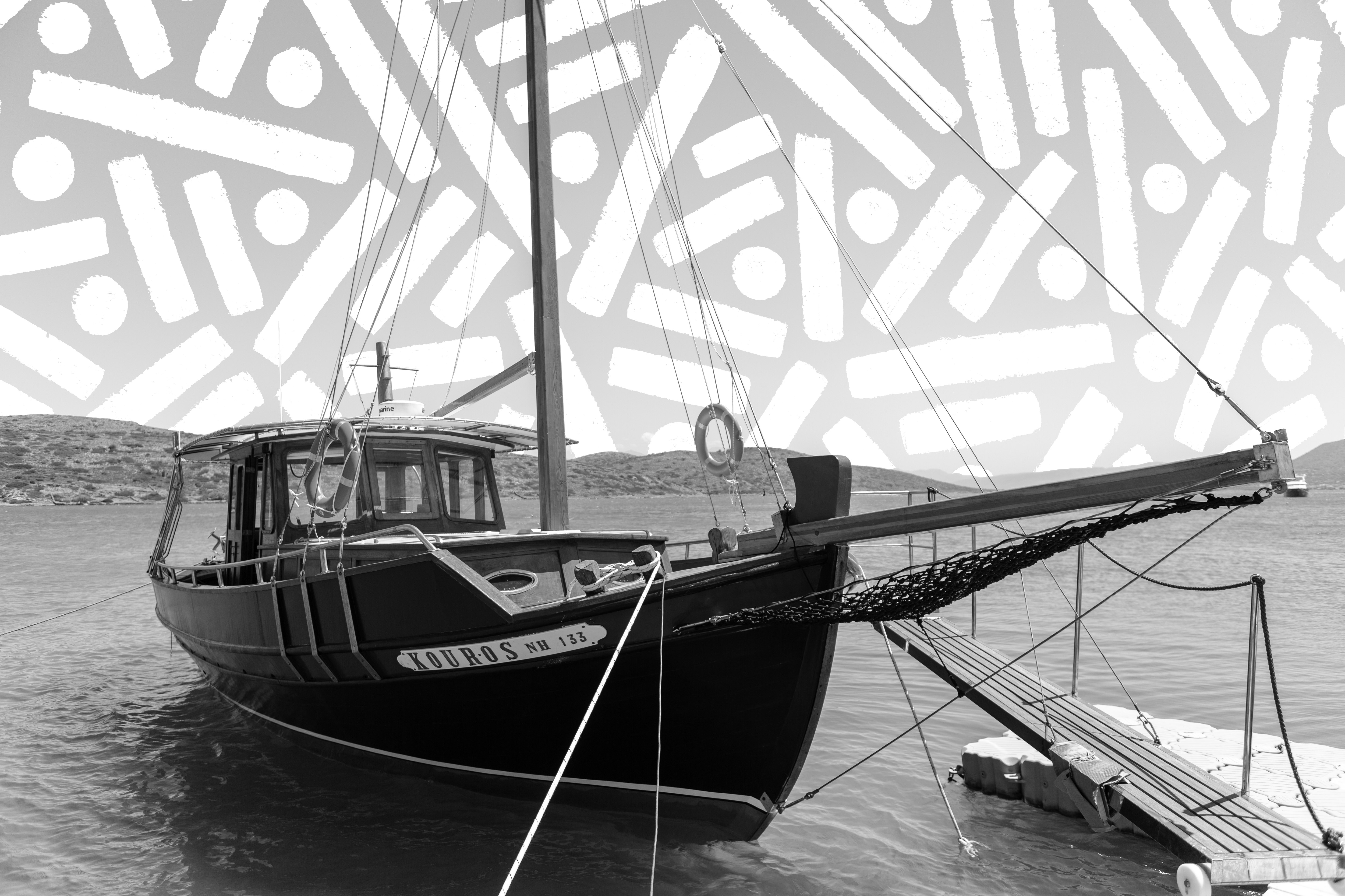 “Convergence at Rest” by Pipe Yanguas, a black-and-white photograph of a sailboat moored along the coast of Crete beneath a geometric sky of dots and lines.