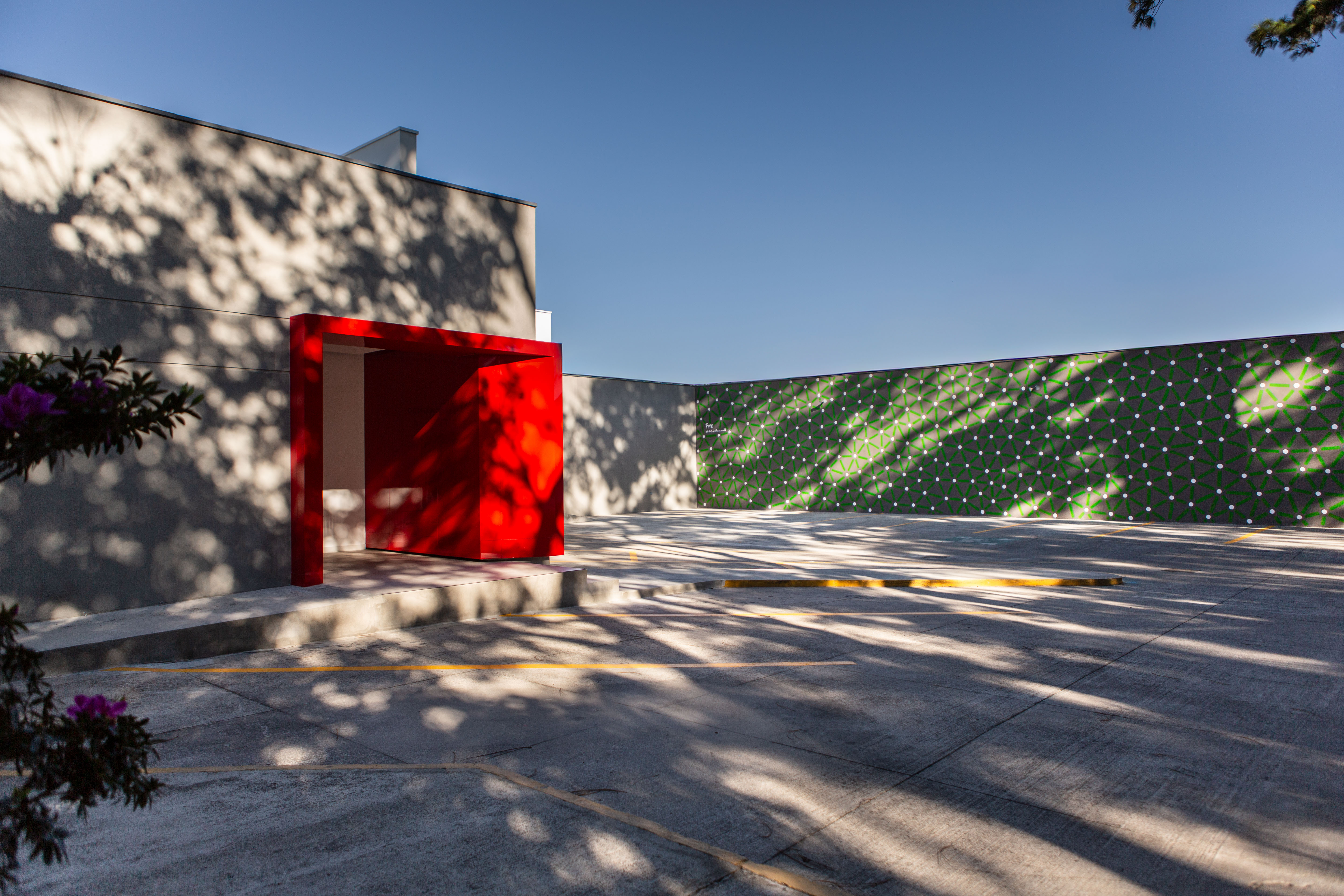 Roots: Courtyard with a red doorway and a long green-and-white patterned wall beneath a blue sky.